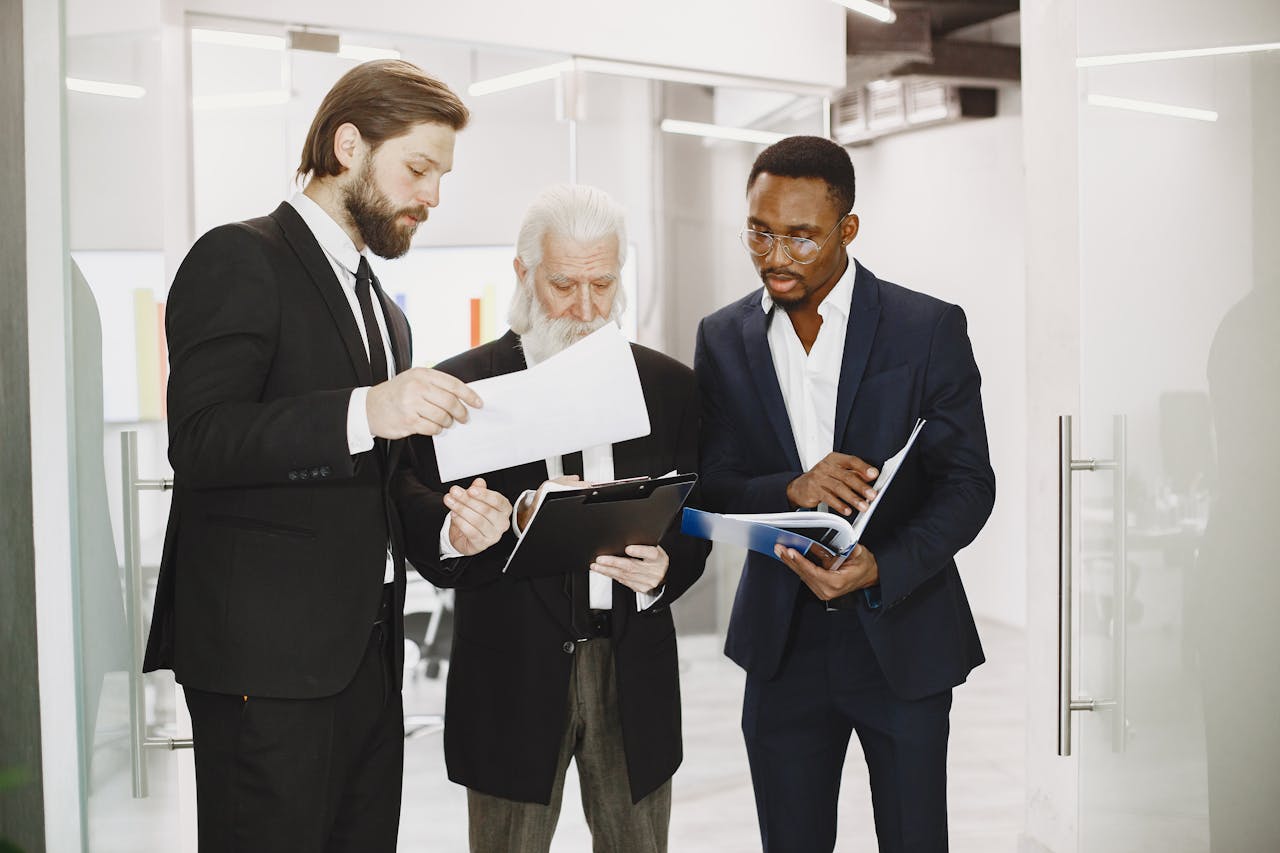 Three diverse businessmen in suits collaborate over documents in a modern office setting.